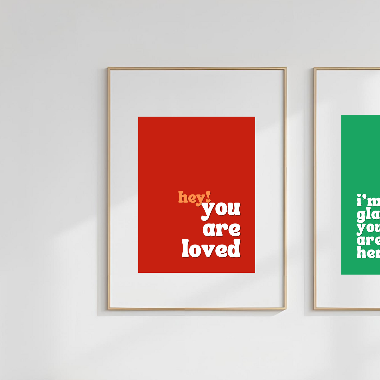 Two framed prints on a white wall, one red and one green, with motivational text.