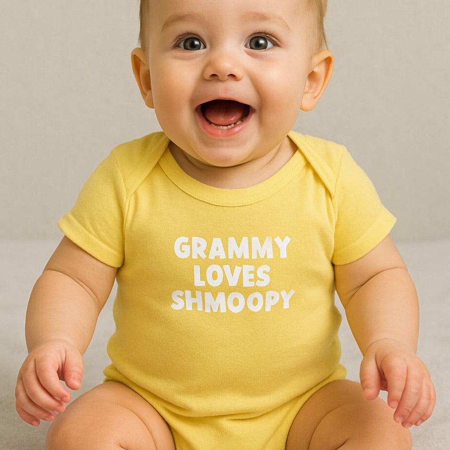 Baby wearing a yellow onesie with 'GRAMMY LOVES SHMOOPY' text on a neutral background